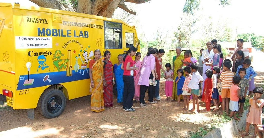 A group of standing in front of bus and giving books to the kids